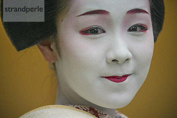 Porträt einer Maiko  einer Geisha-Lehrling in Kyoto und Westjapan. Ihre Arbeit besteht darin  bei Banketten und Festen für die Gäste Lieder und Tänze aufzuführen und auf dem Shamisen oder anderen traditionellen japanischen Instrumenten zu spielen. Maiko sind in der Regel zwischen 17 und 20 Jahre alt und erlangen nach einer gewissen Ausbildungszeit den Status einer Geisha. Diese Ausbildung dauert in der Regel einige Monate bis zu einem Jahr oder zwei Jahren  wobei Lehrlinge  die zu alt sind  um sich als Maiko zu kleiden  trotz ihrer Ausbildung die Stufe der Geisha überspringen können; Kyoto  Japan