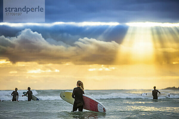 Ein wunderschöner Sonnenaufgang begrüßt die Surfer  die sich auf das morgendliche Surfen vorbereiten und hinauspaddeln; Arrawarra  New South Wales  Australien