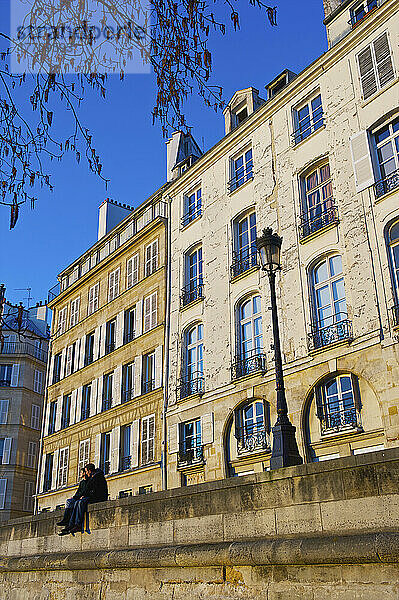 Ein Paar sitzt zusammen auf einer Mauer neben einem Laternenpfahl vor einem Wohnhaus; Paris  Frankreich