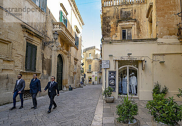 Drei Männer spazieren auf dem Stadtplatz vorbei an Geschäften im historischen Zentrum von Lecce  Italien; Lecce  Apulien  Italien