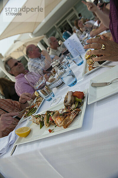 Ein Tisch mit Touristen  die ein Mittagessen im Freien mit aufgespießten Meeresfrüchten genießen; Djerba  Tunesien