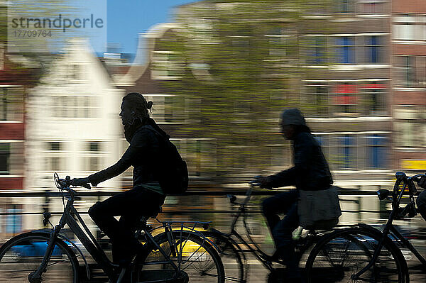 Silhouette von Radfahrern  die an Grachten und Giebelhäusern vorbeifahren; Amsterdam  Holland