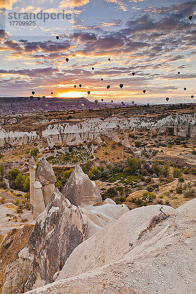 Eine Fülle von Heißluftballons fliegen über die zerklüftete Landschaft des Honigtals bei Sonnenuntergang; Kappadokien  Türkei