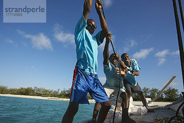 Männer arbeiten zusammen  um ein Segel auf einem Segelboot zu hissen; Insel Vamizi  Mosambik