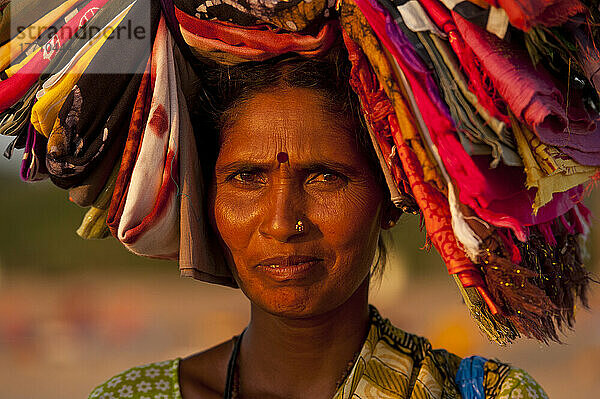 Frau verkauft indische Tücher am Strand in der Abenddämmerung; Candolim  Goa  Indien