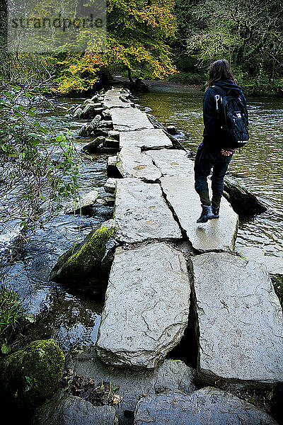 Tourist beim Überqueren der Tarr Steps  einer prähistorischen Klappbrücke über den Fluss Barle  Exmoor National Park; Somerset  England