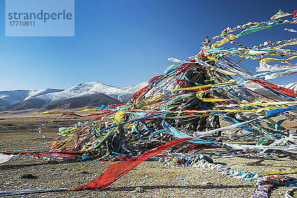 Bunte tibetische Gebetsfahnen (Lung Ta) unter dem starken Wind mit weißen Bergspitzen im Hintergrund; Provinz Qinghai  Tibet