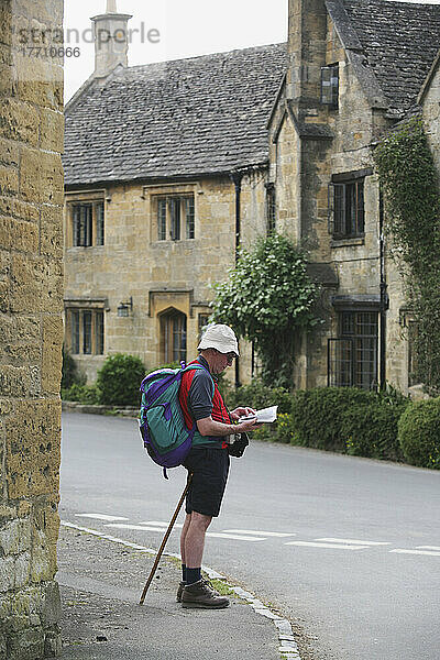 Wanderer beim Überprüfen der Wegbeschreibung im Dorf Stanton mit honigfarbenen Cotswold-Kalkstein-Gebäuden im Hintergrund; Gloucestershire  England