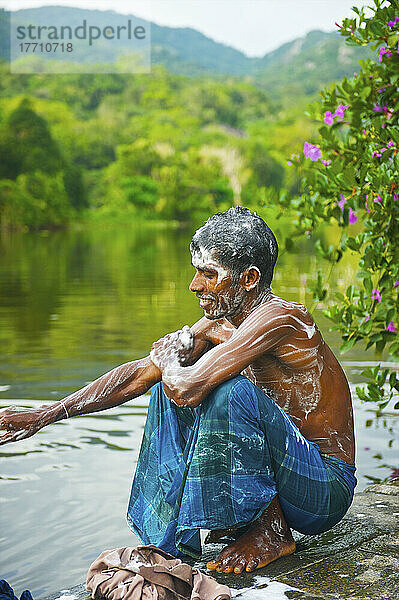 Ein junger Mann hockt am Rande des Wassers  bedeckt mit Seifenlauge; Ulpotha  Embogama  Sri Lanka