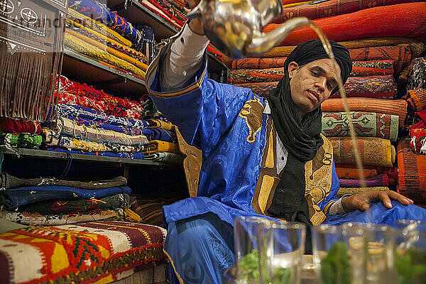Ein traditionell gekleideter Mann aus einem Berberdorf schenkt in einem Teppichgeschäft in Erfoud  Marokko  marokkanischen Tee ein; Erfoud  Marokko