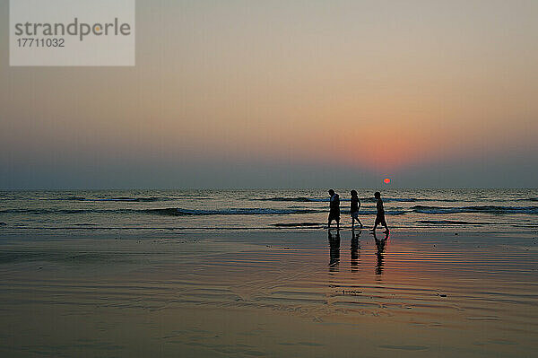 Indische Familie  die in der Abenddämmerung am Strand spazieren geht; Goa  Indien