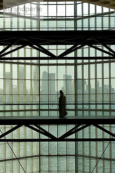 Silhouette eines Paares  das an einem großen Fenster im Museum für islamische Kunst vor der modernen Stadtsilhouette von Doha vorbeigeht; Doha  Katar