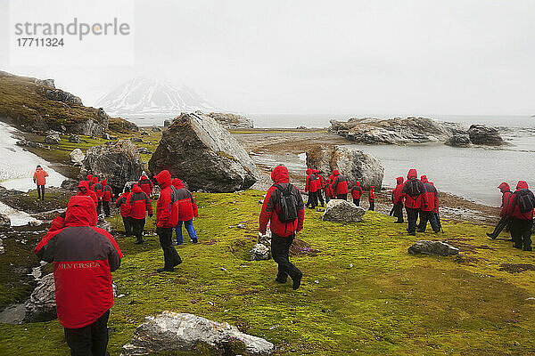 Touristen in passenden roten Mänteln wandern um eine Insel; Svalbard  Norwegen