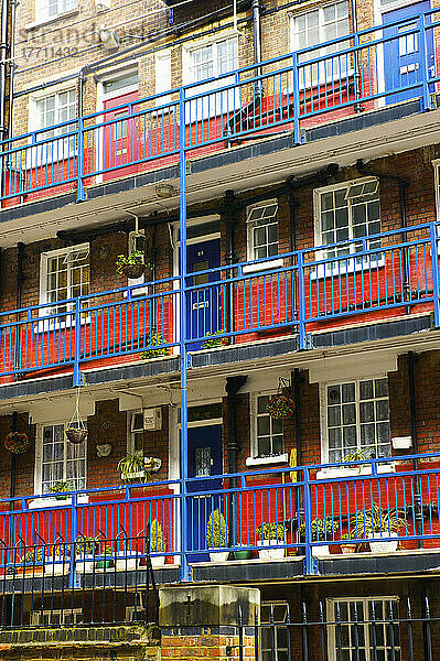 Ein Wohngebäude aus Backstein mit einem blauen Balkongeländer und Türen sowie einem roten Streifen auf der unteren Hälfte jeder Wand; London  England
