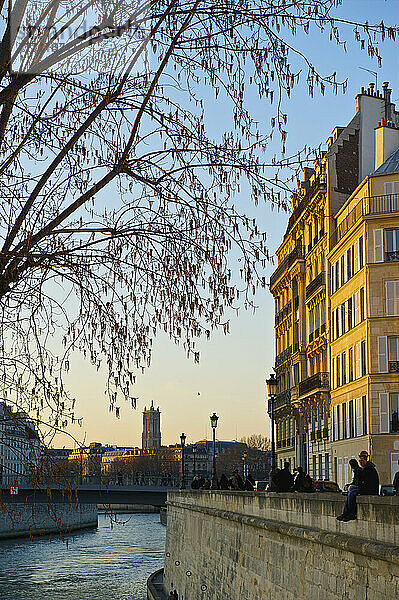 Ein Paar sitzt zusammen an einer Kanalmauer mit Sonnenuntergang Sonnenlicht auf die Gebäude gegossen; Paris  Frankreich