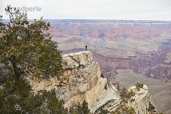 Weitwinkellandschaft eines Touristen mit erhobenen Armen  der auf einem Felsvorsprung des Grand Canyon fotografiert wird; Arizona  Vereinigte Staaten von Amerika