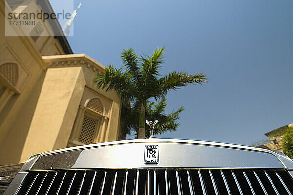 Detail eines verchromten Rolls Royce unter einer Palme und einem traditionellen Hotel im arabischen Stil mit dem Burj Khalifa dahinter; Dubai  Vereinigte Arabische Emirate