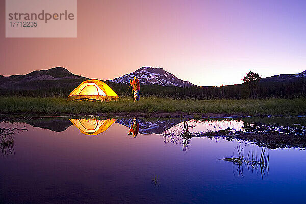 Mann mit Kamera und Stativ beim Fotografieren der Schönheit Oregons bei Sonnenaufgang neben dem Zelt am Sparks Lake  mit South Sister und Broken Top im Hintergrund  Oregon Cascades; Oregon  Vereinigte Staaten von Amerika