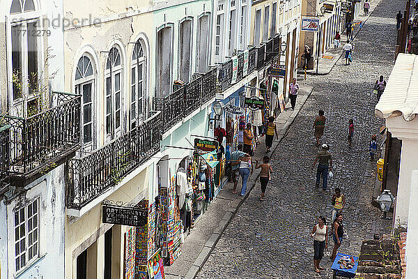 Gepflasterte Einkaufsstraße im historischen Zentrum der alten Kolonialstadt  mit ausgestellten Gemälden und Kleidungsstücken und vorbeischlendernden Kunden; Salvador  Brasilien
