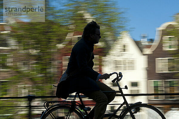 Silhouette eines Radfahrers  der an einer Gracht und Giebelhäusern vorbeifährt; Amsterdam  Holland