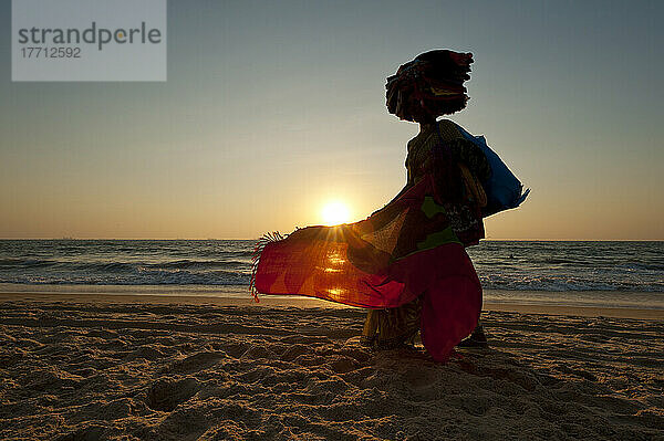 Silhouette einer Frau  die am Strand in der Abenddämmerung indische Tücher verkauft; Candolim  Goa  Indien