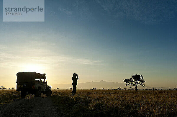 Silhouette einer Frau  die durch ein Fernglas vor dem Berg Kenia in der Morgendämmerung schaut  Ol Pejeta Conservancy; Kenia