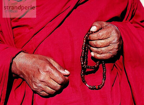 Mönch in roter Robe hält Gebetsperlen