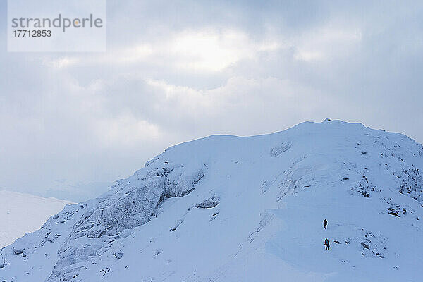 Zwei Menschen nähern sich dem Gipfel des Beinn Dorain bei verschneiten  winterlichen Bedingungen in der Nähe der Bridge of Orchy; Argyll und Bute  Schottland