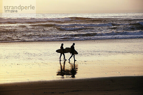 Paar trägt Surfbretter am Strand in Silhouette