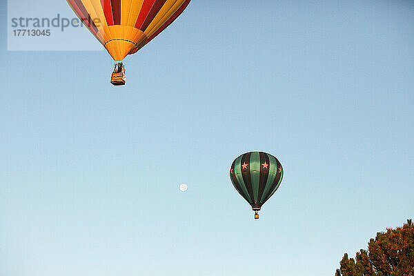 Ein paar Heißluftballons steigen in der Nähe von Bäumen mit dem Mond im Hintergrund gegen einen klaren Himmel auf; Prosser  Washington