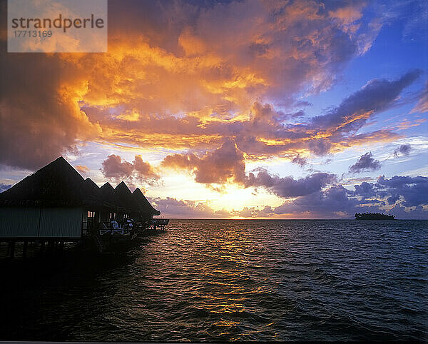 Sonnenuntergang über einer kleinen Insel auf den Malediven mit Unterkünften auf der linken Seite; Malediven