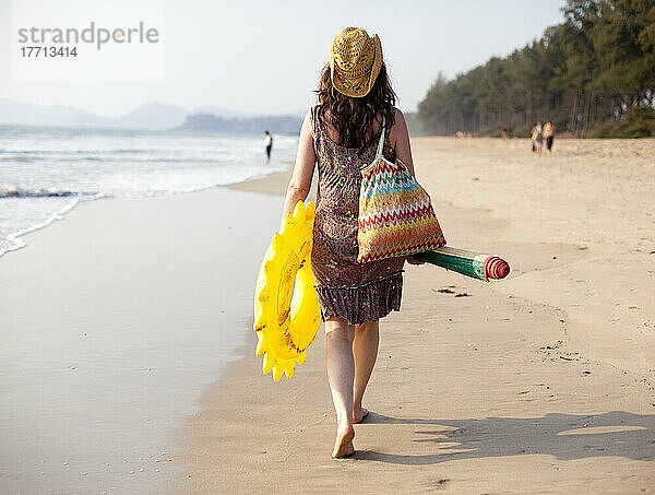 Eine Mutter geht nach einem Tag am Turtle Beach  Goa  Indien  mit Schlauchbooten und Strandmatte vom Strand zurück.