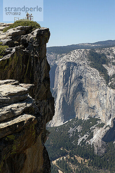 Mit dem El Capitan in der Ferne stehen Wanderer am Gipfel des Taft Point Wanderwegs an einem Geländer und blicken über die Kante auf das Yosemite Valley; Yosemite National Park  Kalifornien