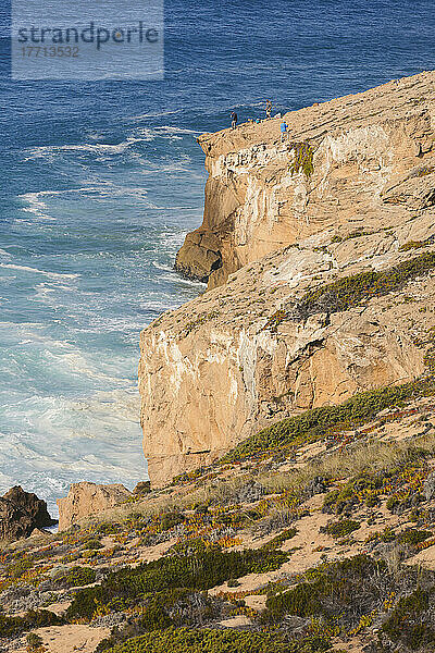 Touristen stehen auf einem abfallenden  zerklüfteten Bergrücken mit Blick auf die Klippen und die Küste des Atlantischen Ozeans  Praia de Monte Clerigo und den Naturpark Südwest-Alentejo und Vicentiner Küste; Algarve  Portugal