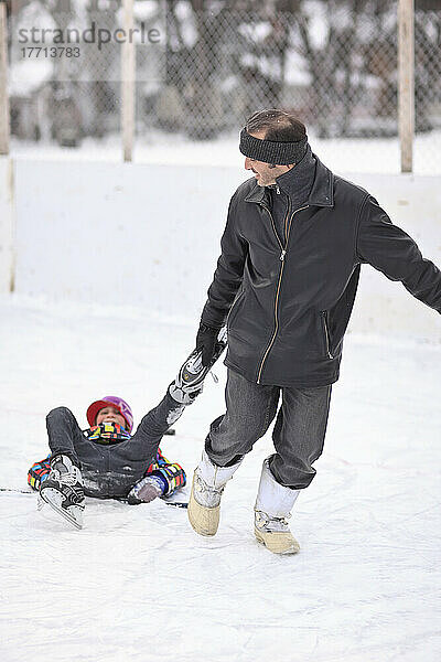 Vater  der seinen Sohn an seinen Schlittschuhen auf einer Eisbahn im Freien zieht. Winnipeg  Manitoba  Kanada.