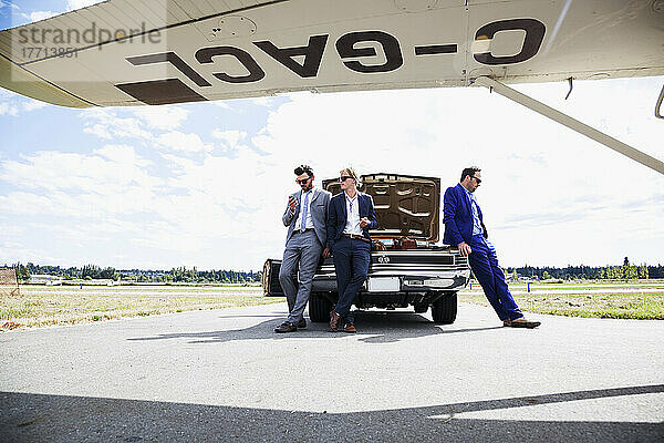 Drei Geschäftsleute lehnen sich an ein Auto mit offenem Kofferraum und einem Flugzeug; Langley  British Columbia  Kanada