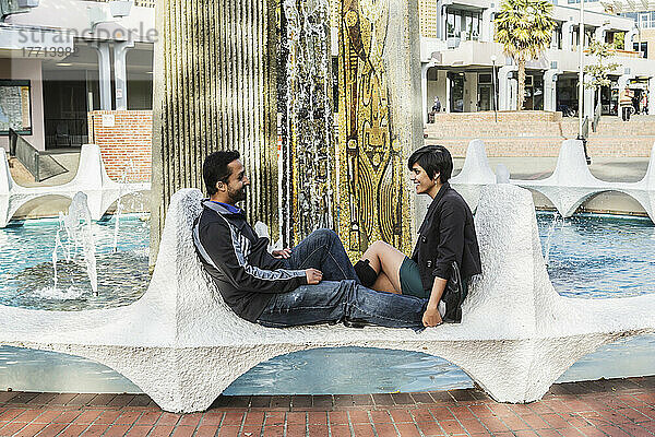 Ein junges indischstämmiges Paar entspannt sich an den keramischen Flossen des Centennial Square Fountain; Victoria  Vancouver Island  British Columbia