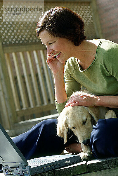 Frau am Telefon mit Laptop und Welpe