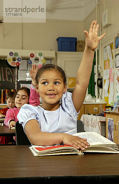 Sechs Jahre altes Mädchen hebt die Hand an ihrem Schreibtisch in einem Klassenzimmer