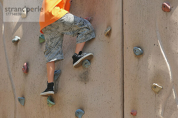 Junger Junge klettert auf dem Spielplatz an der Felswand