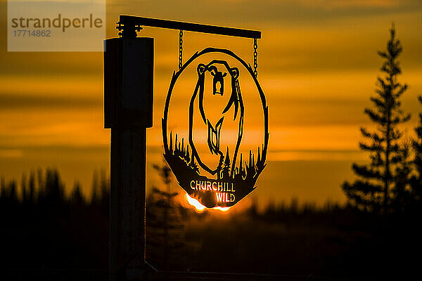 Oranger Sonnenaufgang  der durch das Metallschild für Churchill Wild  Polar Bear Lodge  scheint; Churchill  Manitoba  Kanada