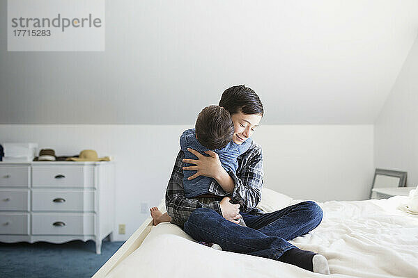 Brüder umarmen sich auf einem großen Bett zu Hause  der jüngere Bruder hat das Down-Syndrom; Victoria  British Columbia  Kanada