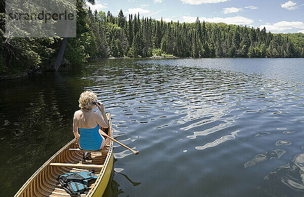 Ältere Frau  die mit ihrem Handy telefoniert  während sie Kanu fährt  Algonquin Park  Ontario