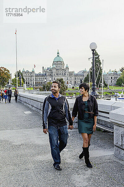 Ein junges indianisch-ethnisches Paar  das an der Uferpromenade vor den Parlamentsgebäuden spazieren geht; Victoria  Vancouver Island  British Columbia