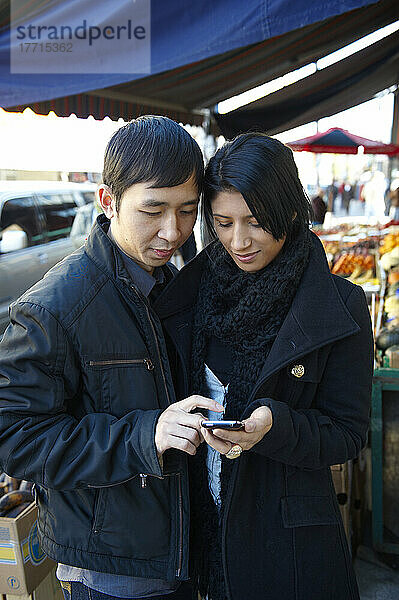 Junges Paar benutzt ein Mobiltelefon im Kensigton Market  Toronto  Ontario