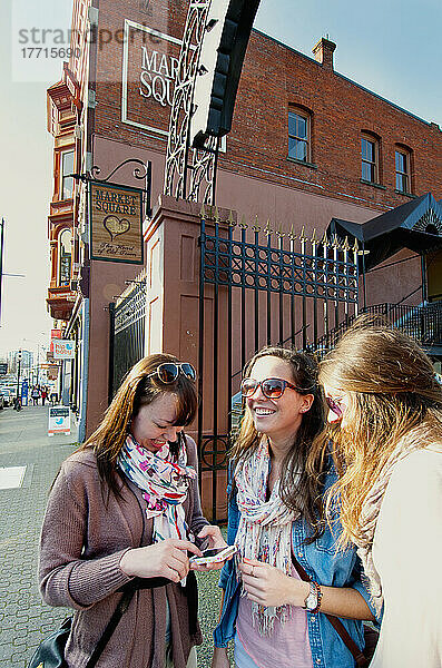 Junge Frauen  die am Marktplatz in der Lower Johnson Street den Weg ihres Telefons überprüfen; Victoria  Vancouver Island  British Columbia  Kanada