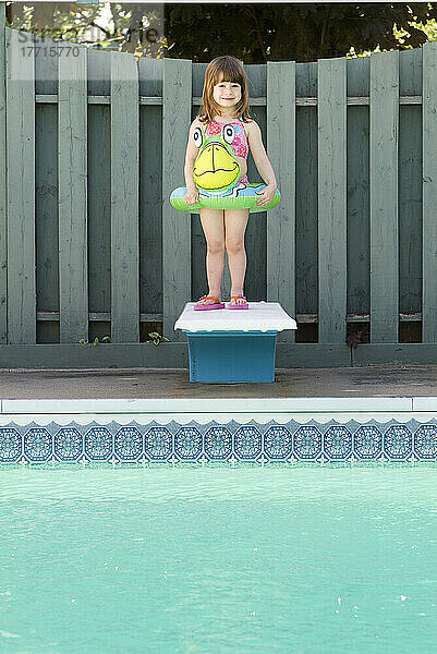 Kleines Mädchen lächelnd stehend auf einem Sprungbrett über einem Pool