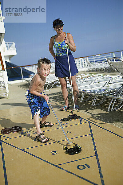 Junger Junge mit Mutter spielen Shuffle Board auf Deck des Kreuzfahrtschiffes