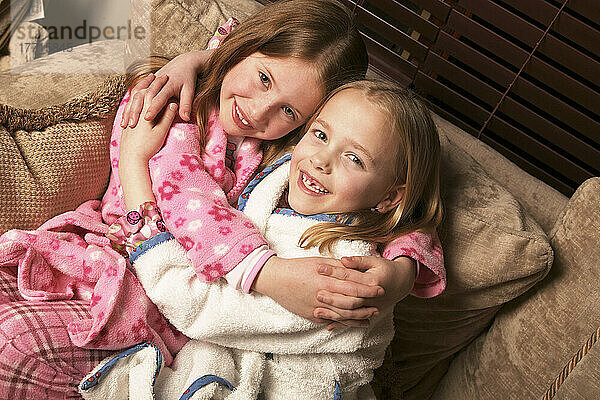 Zwei junge Mädchen umarmen auf Couch in Pyjamas