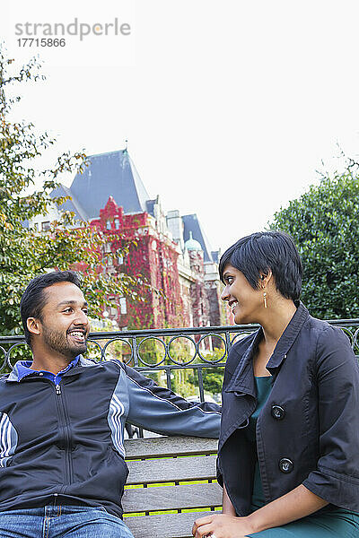 Ein glückliches junges indianisch-ethnisches Paar sitzt zusammen auf einer Parkbank; Victoria  Vancouver Island  British Columbia